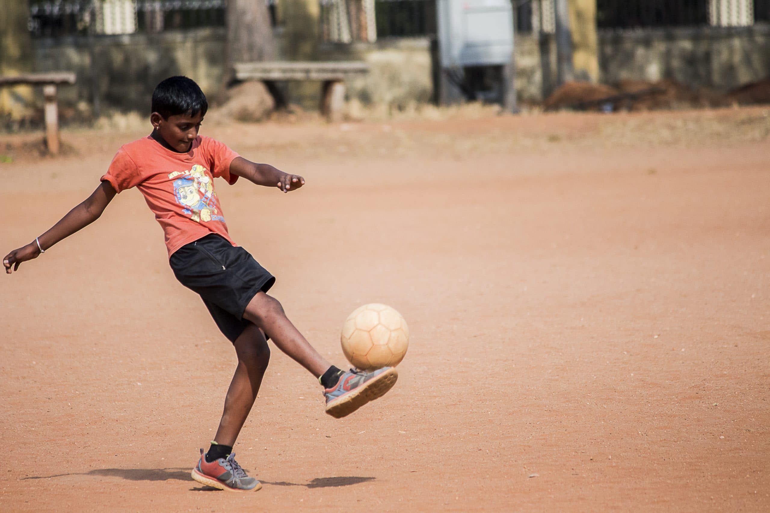 A young player controlling a football on a rough outdoor field