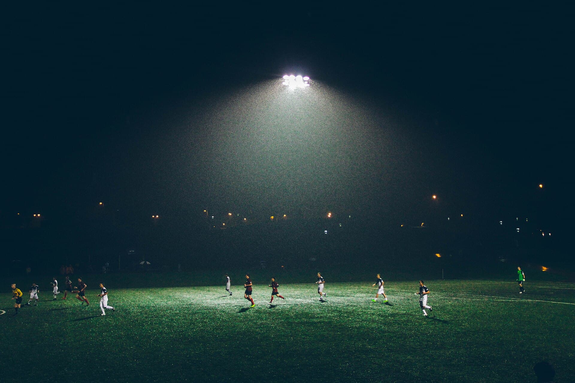 A football match played at night in heavy rain beneath bright stadium floodlights